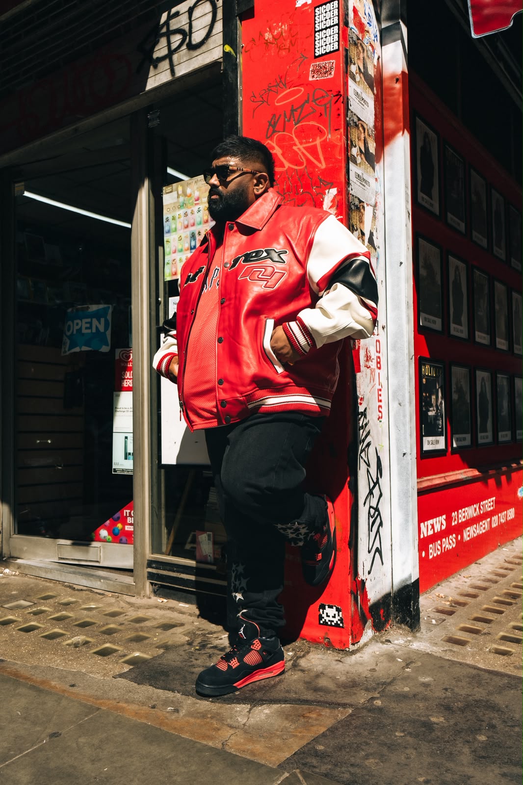 DJK leaning beside a vivid red London exterior in premium streetwear.