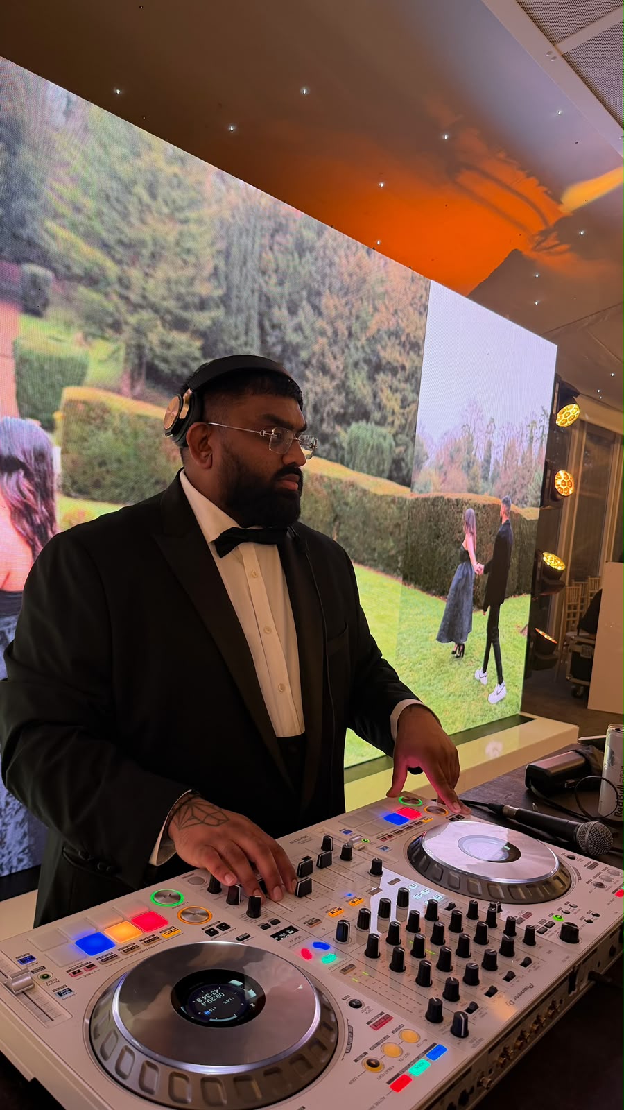 DJK performing behind white DJ decks with LED wall visuals.